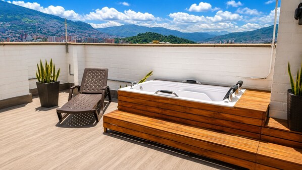 A rooftop terrace with a wooden deck, a hot tub, and two lounge chairs. - penthouse jacuzzi rooftop fun in the sun (Medellín)