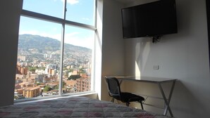 Un dormitorio con un ventanal grande, una cama, un escritorio y un televisor.