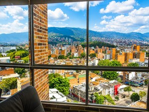 A cityscape view from a window with a brick wall and a view of a densely built urban area with mountains in the background. - penthouse jacuzzi rooftop fun in the sun (Medellín)