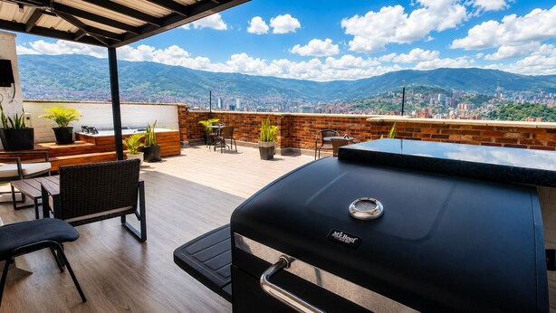 An outdoor patio with a grill, seating area, and a view of a cityscape and mountains.