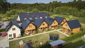 A cluster of wooden cabins with sloped roofs, surrounded by a well-maintained lawn and a forested area in the background. - Cottage in Plesna Near Sandy Beach (gmina Będzino)