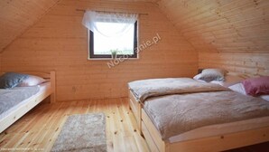 A small, cozy attic bedroom with two single beds, a window with a sheer curtain, and a wooden ceiling. - Cottage in Plesna Near Sandy Beach (gmina Będzino)