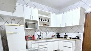 Una cocina con armarios blancos, microondas, cafetera y refrigerador.