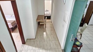 Un pasillo estrecho con una cama al fondo, una silla y una mesita.