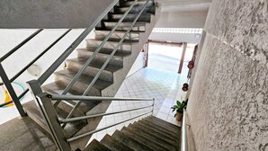 Una escalera con barandillas metálicas y escalones de piedra que conduce a un espacio abierto con suelo de baldosas y una planta en maceta.