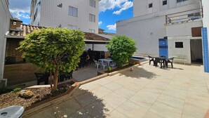 Un patio con piso de baldosas, mobiliario exterior y dos árboles pequeños.