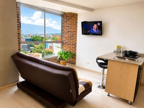 A modern living room with a large window, a sofa, a dining area with a table and chairs, and a flat-screen TV mounted on the wall. - apartament with the best views  (Medellín)