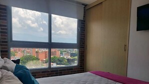 A bedroom with a large window, a bed with white and teal bedding, and a view of a cityscape. - apartament with the best views  (Medellín)
