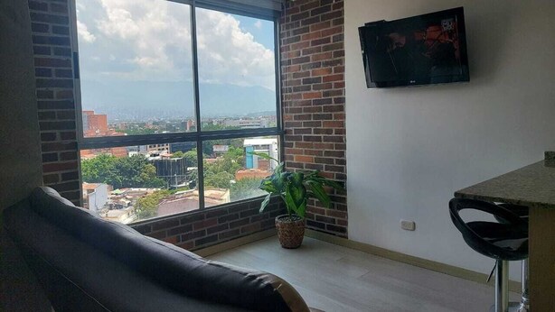 A room with a large window, a black leather chair, a small potted plant, and a TV mounted on the wall. - apartament with the best views  (Medellín)