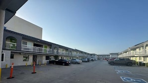 A parking lot with multiple cars, a building with a balcony, and a clear sky.
