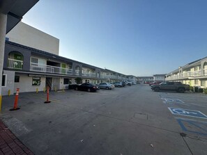 A parking lot with multiple cars, a building with a balcony, and a clear sky.
