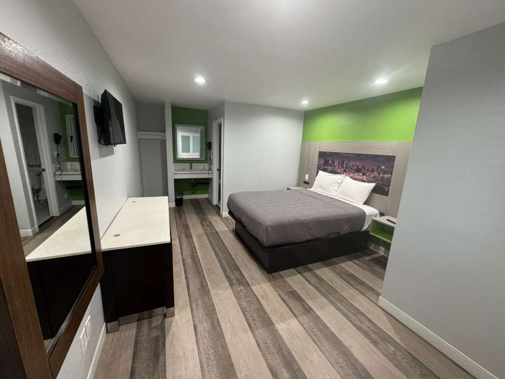 Une chambre à coucher avec un lit, une table de chevet, un miroir, une télévision et un mur vert.