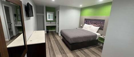 Une chambre à coucher avec un lit, une table de chevet, un miroir, une télévision et un mur vert.