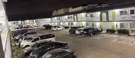 A parking lot with multiple cars and a building with green doors and white walls.