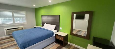 Un dormitorio con una cama, una mesita de noche y un espejo en una pared verde.