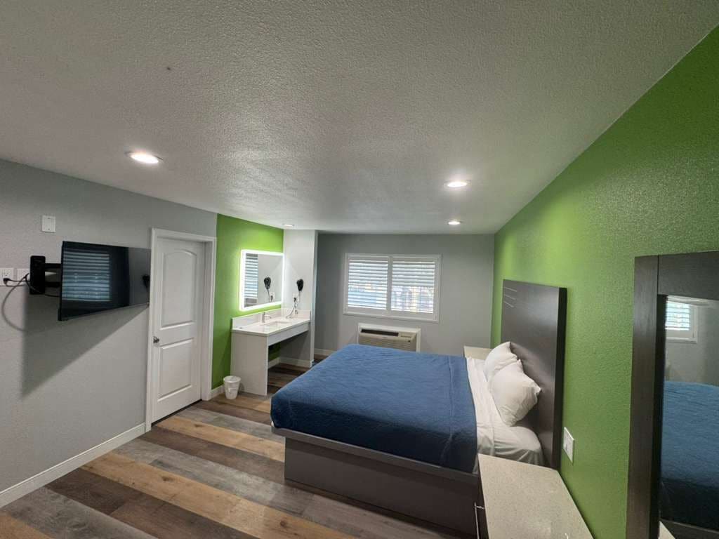 A bedroom with a bed, a vanity, a television, and a window.