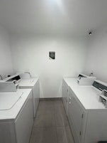 Un lavadero con dos lavadoras y una secadora, un cartel que indica su función, y una lámpara instalada en el techo.