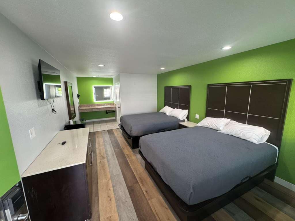 A room with two beds, a desk, a mirror, and a television.