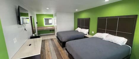A room with two beds, a desk, a mirror, and a television.