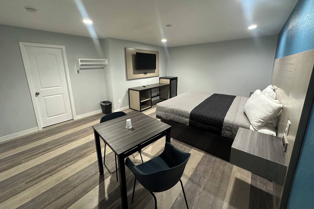Een moderne hotelkamer met een bed, een bureau, een stoel, een televisie en een kleine prullenbak.