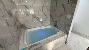 A modern bathroom with a marble-tiled wall and floor, a freestanding bathtub, and a visible showerhead. - Palm Motel - Rosemead (Rosemead)