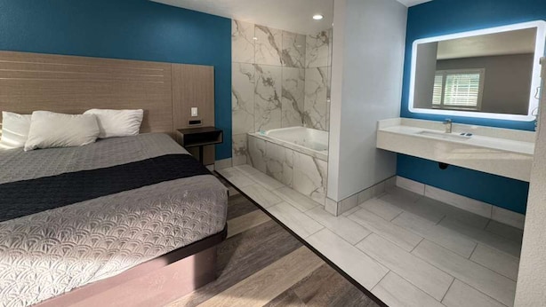 A modern bedroom with a large bed, a separate bathroom with a bathtub, and a vanity with a mirror. - Palm Motel - Rosemead (Rosemead)