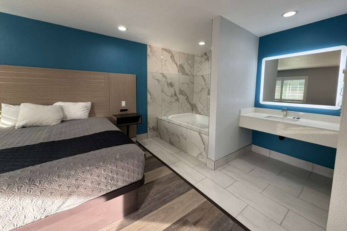 Een moderne slaapkamer met een groot bed, een aparte badkamer met een badkuip en een wastafel met spiegel.