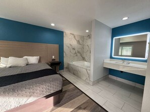 Une chambre moderne avec un grand lit, une salle de bain séparée avec une baignoire et une coiffeuse avec un miroir.