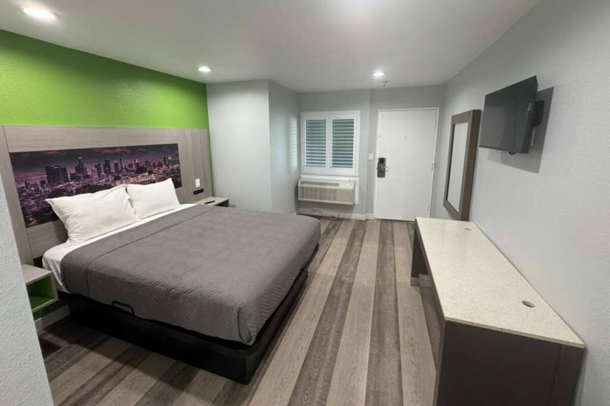 Hotelkamer met een bed, bureau, televisie, raam met zonwering en een airconditioning.