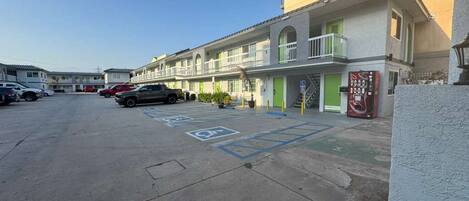 Un estacionamiento con espacios reservados para discapacitados, un edificio con varios balcones y una máquina expendedora en la acera.