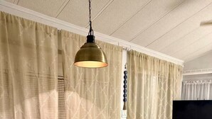 Et værelse med et arbejdsbord, en hængende lampe, et fladskærms-tv og mønstrede gardiner.