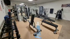 Et fitnessrum med forskellig træningsudstyr, herunder håndvægte, bænke og vægtmaskiner.