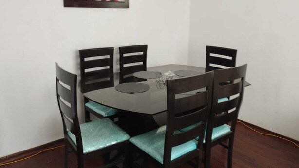 Un coin repas avec une table ronde et quatre chaises, chacune agrémentée d’un coussin de couleur turquoise. Deux œuvres d’art encadrées sont accrochées au mur au-dessus de la table.