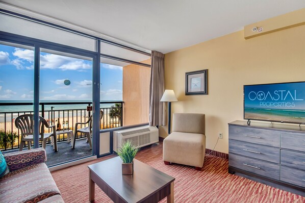 A hotel room with a balcony, a TV, a sofa, a coffee table, and a plant.