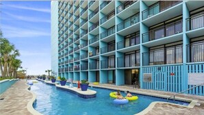 A pool area with a blue building in the background, a tiled walkway, and a 3 FT depth marker. - Oceanfront Sea and Sky Haven! (Myrtle Beach)