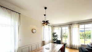 A dining area with a wooden table, chairs, a hanging light fixture, and a view of the outdoors through large windows. - House 5 rooms 6 people, beach and port of Larmor nearby - wifi (LARMOR-PLAGE)
