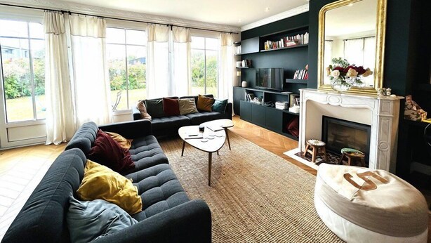 A living room with a dark-colored sofa, a white coffee table, and a fireplace. There are large windows with curtains, a bookshelf, and a mirror above the fireplace. - House 5 rooms 6 people, beach and port of Larmor nearby - wifi (LARMOR-PLAGE)