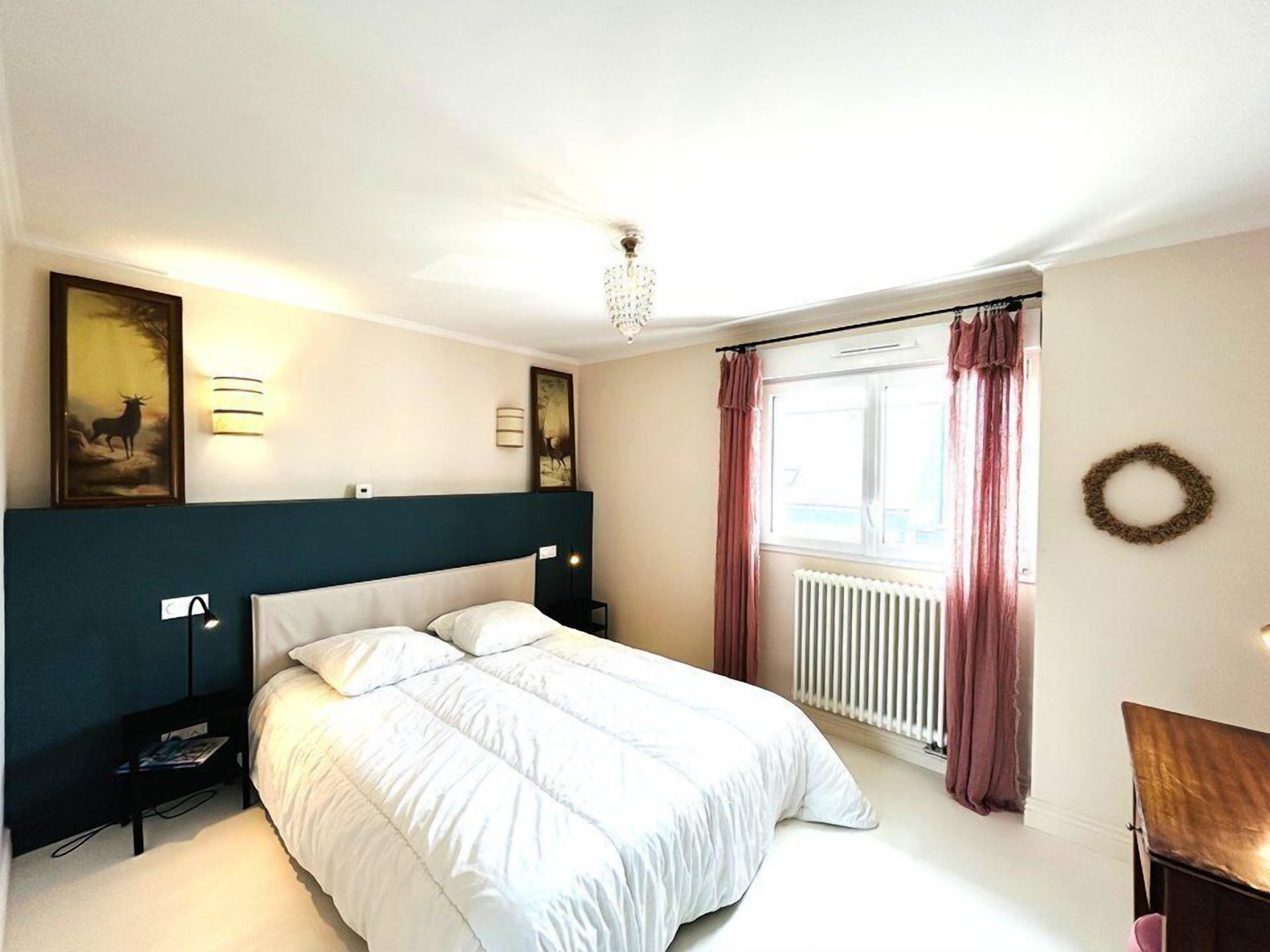 A neatly arranged bedroom with a bed, bedside tables, wall-mounted lamps, and a window with curtains.