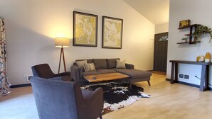 Un salon comprenant un canapé, une table basse, une lampe, un tapis en peau de vache et une carte accrochée au mur.