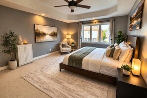 A bedroom with a bed, a ceiling fan, a window with curtains, a bedside table with a lamp, and a painting on the wall. - 8BR Estate by Canterra Stays · Sleeps 20 · Games (Brampton)