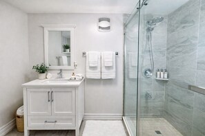 A modern bathroom with a glass-enclosed shower, white cabinetry, a mirror, and a potted plant. - 8BR Estate by Canterra Stays · Sleeps 20 · Games (Brampton)