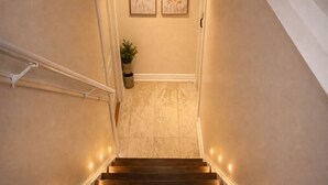 A wooden staircase with a handrail, leading to a landing with two framed artworks and a potted plant. - Two Kitchens · Two Entrances · Sleeps 6 · Pearson ~15 Min (Brampton)