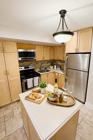 A kitchen with wooden cabinets, stainless steel appliances, a central island with food and drinks, and a hanging light fixture.