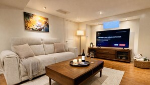 A modern living room with a sofa, coffee table, TV, and a painting on the wall. - Two Kitchens · Two Entrances · Sleeps 6 · Pearson ~15 Min (Brampton)