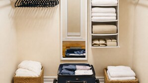 A walk-in closet with a mirror, shelves for folded towels, and a suitcase on a trolley. - Two Kitchens · Two Entrances · Sleeps 6 · Pearson ~15 Min (Brampton)