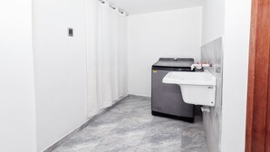 Un baño pequeño y limpio con lavadora, lavamanos y cortina de ducha.