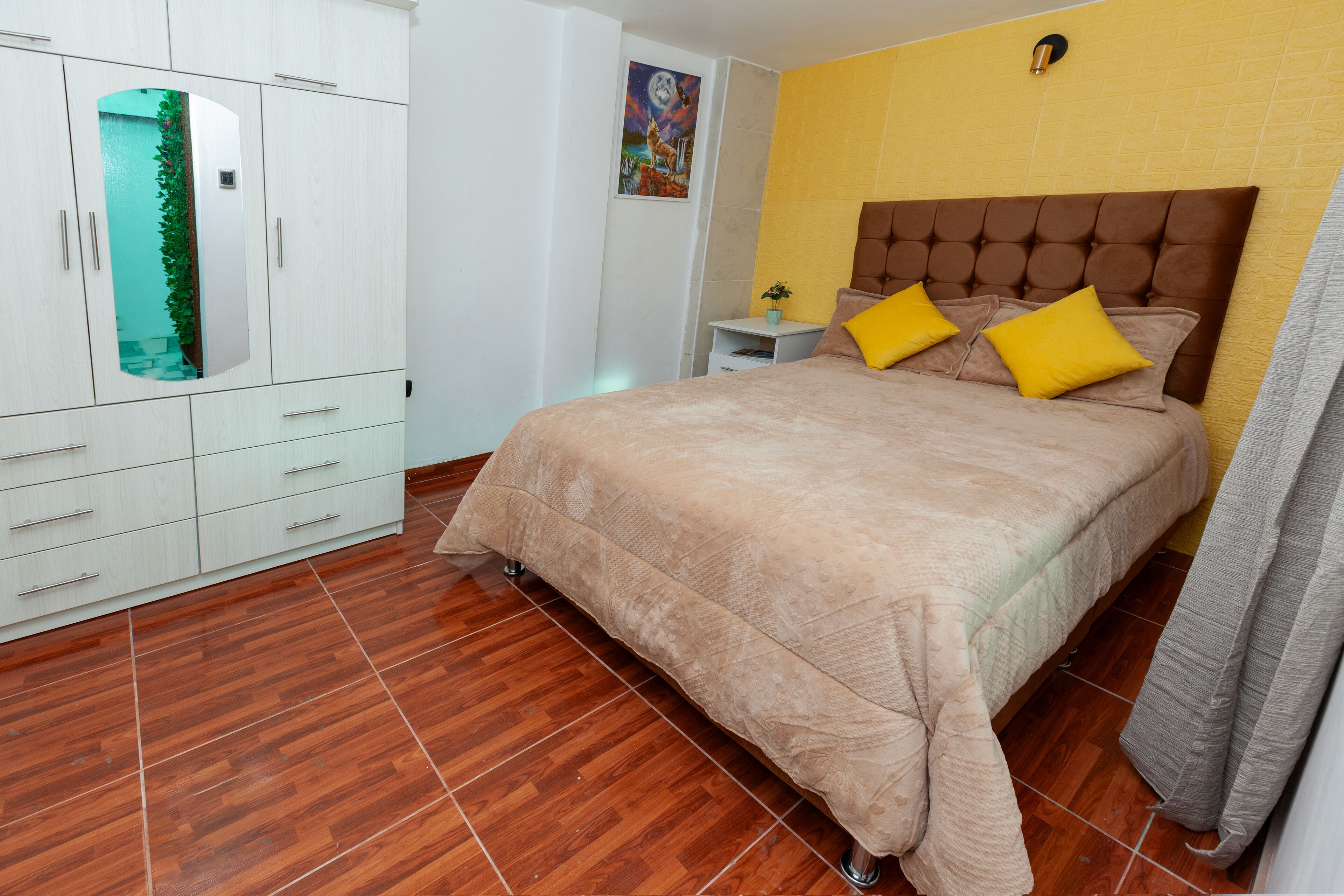 A bedroom with a bed, a wardrobe, a nightstand, and a wall-mounted light fixture.