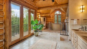 L'intérieur d'une cabane en rondins, avec une grande fenêtre, un ventilateur de plafond, une salle de bain dotée d'une baignoire et une plante en pot.