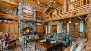 L’intérieur d’une cabane en rondins, avec une cheminée en pierre, des meubles en bois et un balcon.