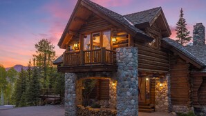 Une cabane en rondins avec des fondations en pierre, un balcon et une cheminée en pierre.